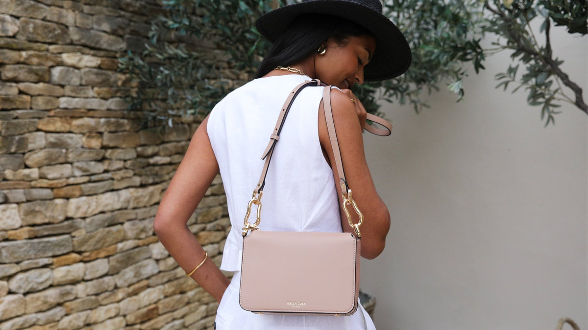 Image of a model in a white suit and black straw hat holding a mocha Margarita crossbody over her shoulder