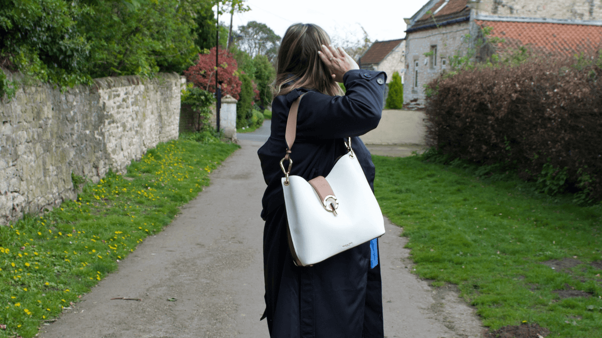 Woman in navy trench coat wearing a Luella Grey London White and Mocha Tote Bag in a pretty village setting 