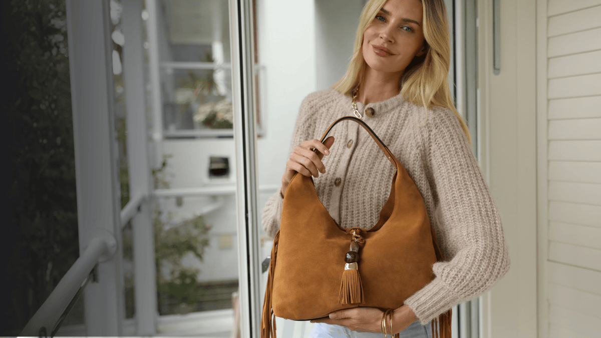 Model holding a slouchy camel suede bag in front of her 