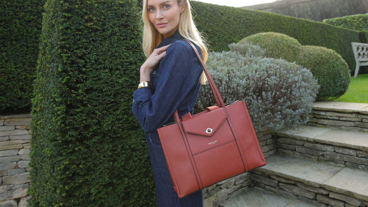 What does your laptop bag say about you - read the blog to find out more. Model in garden in dark denim playsuit carrying the Giselle Laptop Tote in Paprika 