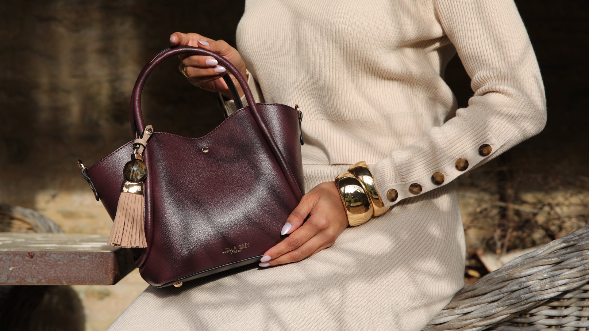 Person holding a purple handbag with a tassel detail, wearing a beige sweater.