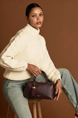 Female model holding Alessia Black Cherry faux leather Bowler Tote by Luella Grey by the grab handles at the top of the bag