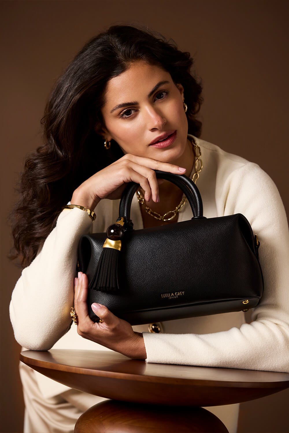 Female model holding Alessia Black faux leather Bowler Tote by Luella Grey by the grab handles and cradling the bag