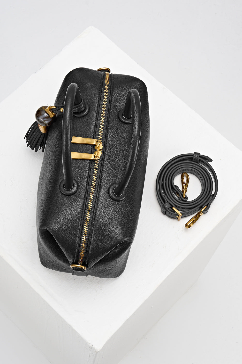 Birds-eye view of Alessia Black faux leather Bowler Tote by Luella Grey with detachable crossbody strap rolled up next to the bag