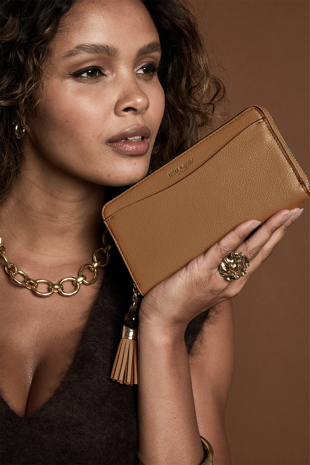 Female model holding Capriana Tan faux leather Large Purse with one hand next to her face