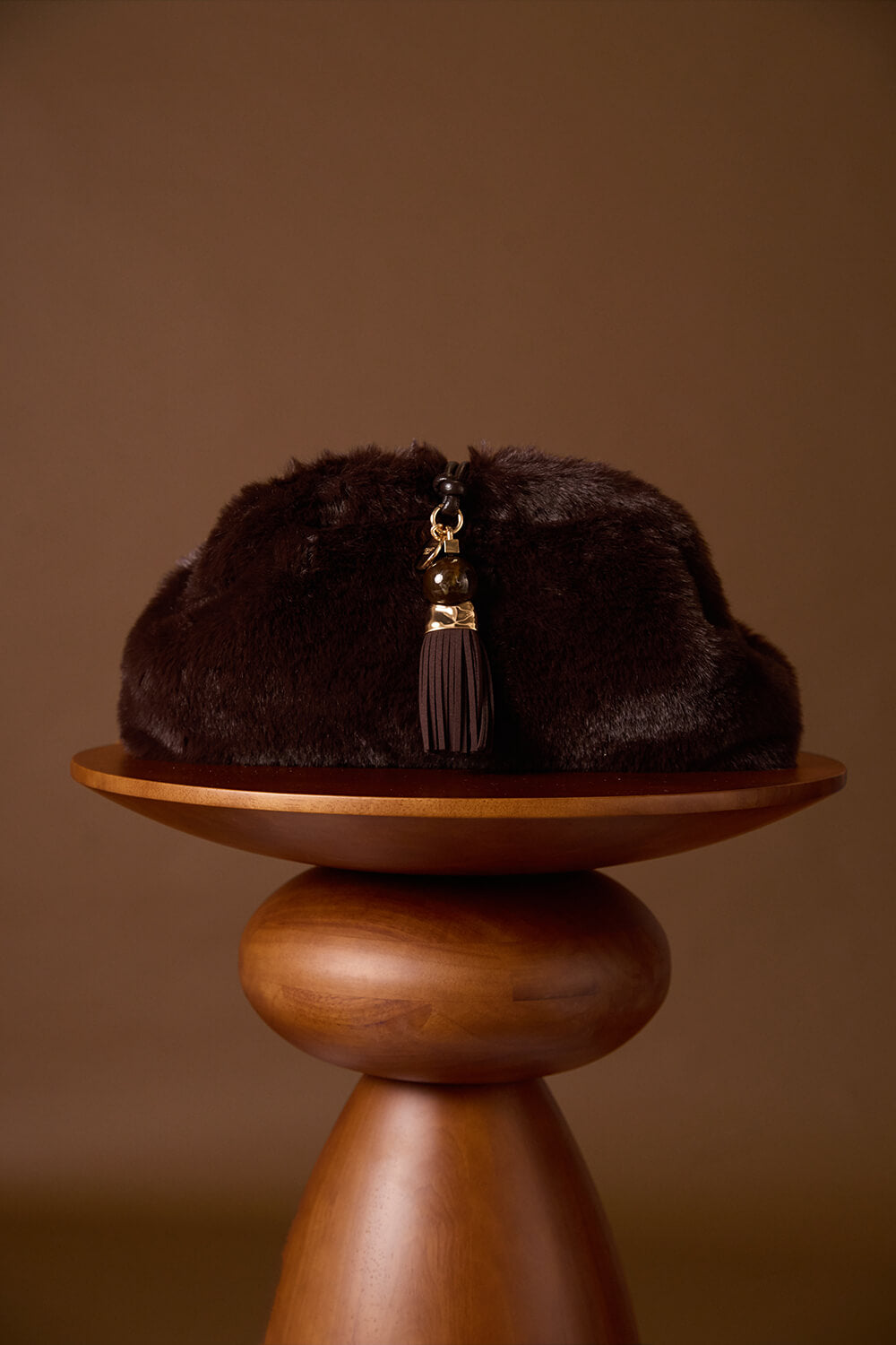 Indigo Chocolate faux fur Oversized Clutch resting on a brown wooden plinth