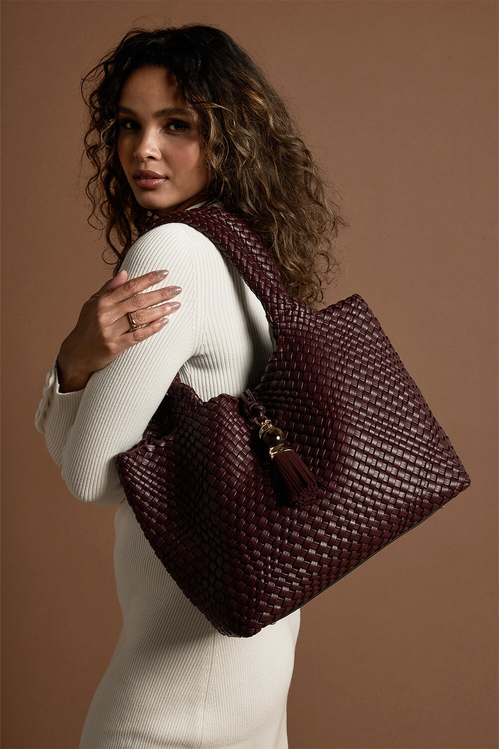 Female model wearing Saskia Black Cherry faux leather Woven Tote over her shoulder with the two shoulder handles