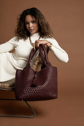 Female model holding Saskia Black Cherry faux leather Woven Tote in  her hand using the two top shoulder handles