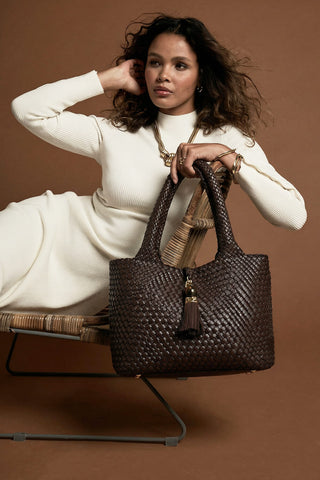 Female model holding Saskia Chocolate faux leather Woven Tote in  her hand using the two top shoulder handles