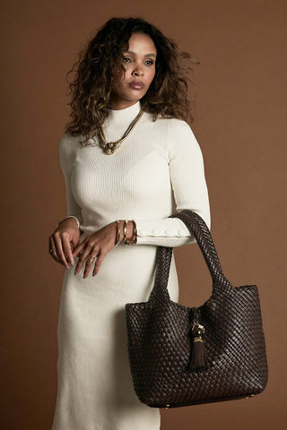 Female model wearing Saskia Chocolate faux leather Woven Tote over her arm with the two shoulder handles