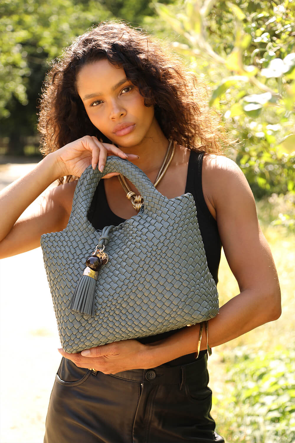 Female model holding Suky Steel Geen faux leather Woven Crossbody by the top grab handles