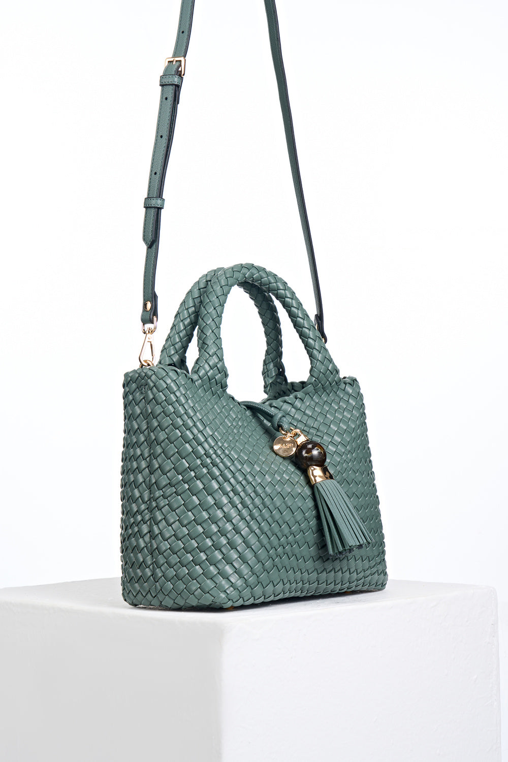 Side view of Suky Steel Green faux leather Woven Crossbody with detachable crossbody strap attached to gold rings on the bag's side
