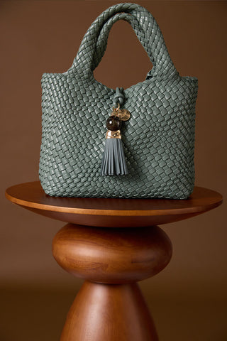 Suky Steel Green faux leather Woven Crossbody on a brown wooden plinth