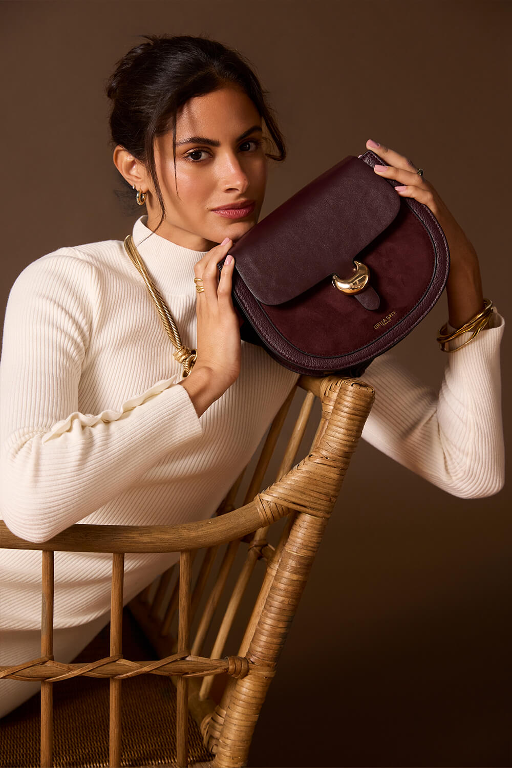 Female model holding Venetia Black Cherry Faux leather Saddle Crossbody in front of her with both hands 