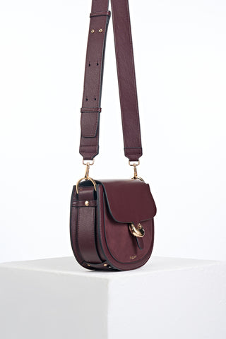 Side view of Venetia Black Cherry Faux leather Saddle Crossbody showing the strap detailing around the bottom of the bag and Cannon Street Clasp detail on the front