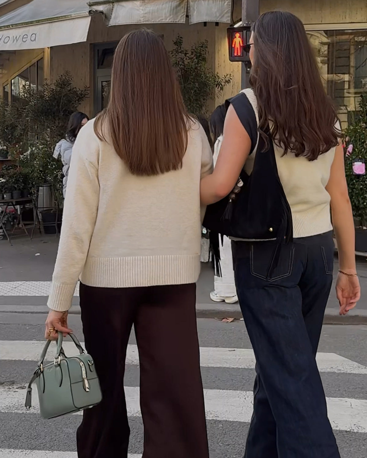 Two women crossing a street at a crosswalk, one holding a green handbag.