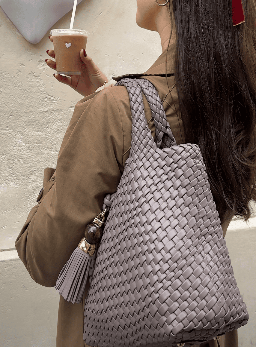 Person holding a woven gray bag and a coffee cup with a heart design.
